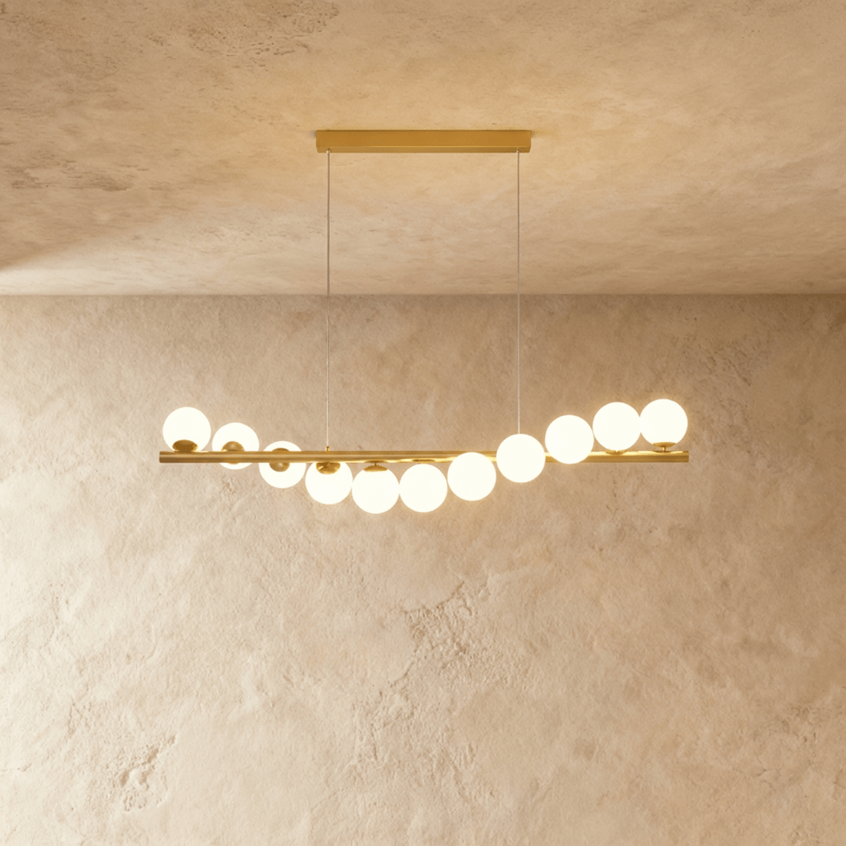Clérachic gold linear chandelier carrying eleven opal white glass globes along a brass bar, lit warm over a limewash wall.