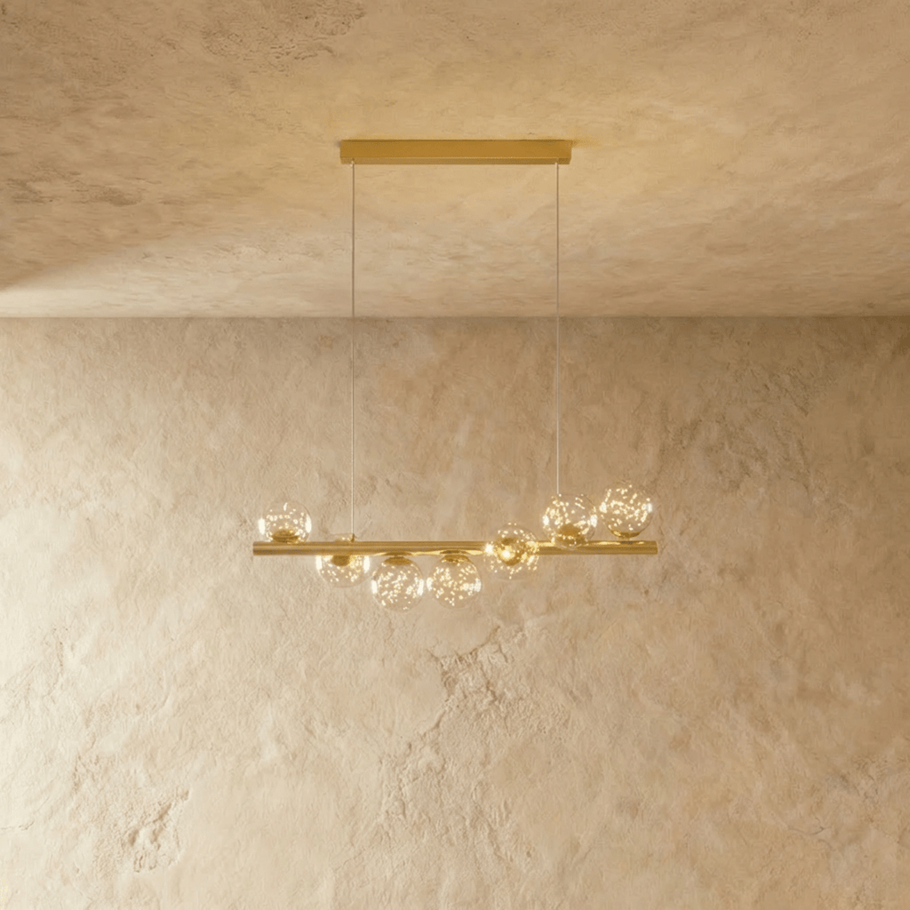 Clérachic gold linear chandelier with seven clear glass globes holding tiny star-like points of light, on a brass bar and wires.