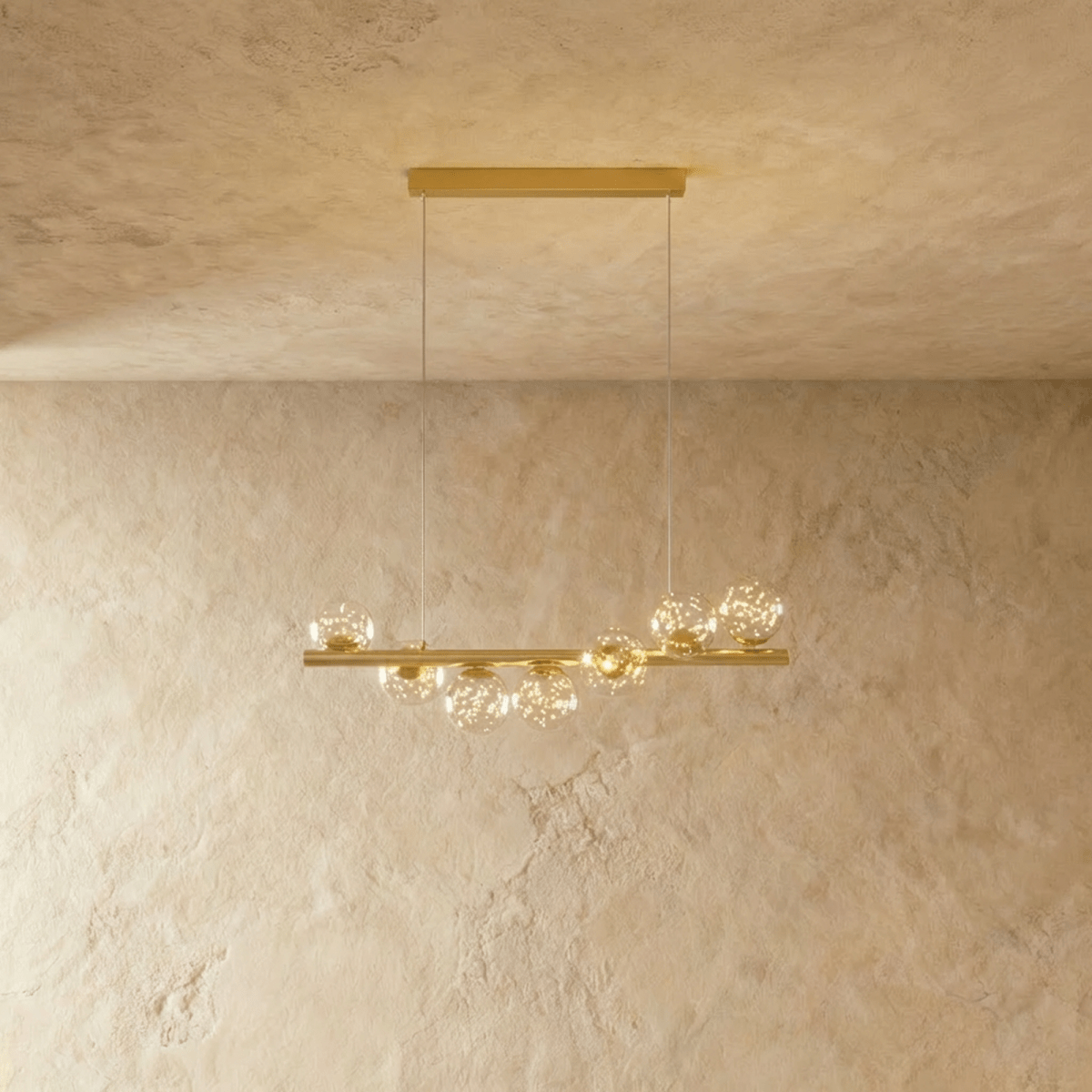 Clérachic gold linear chandelier with seven clear glass globes holding tiny star-like points of light, on a brass bar and wires.