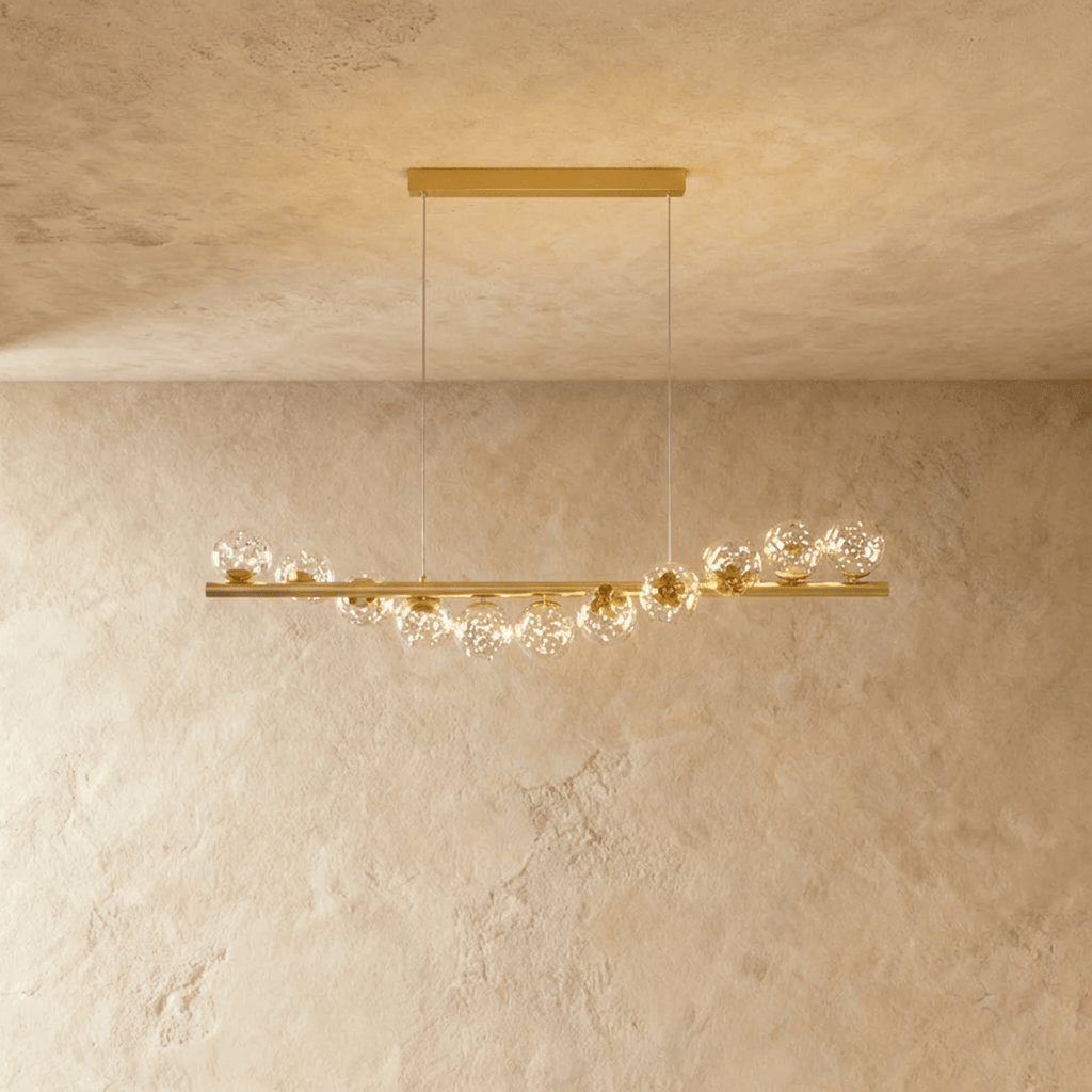 Clérachic gold linear chandelier with eleven clear glass globes sparkling with tiny lights, on a long brass bar and thin wires.