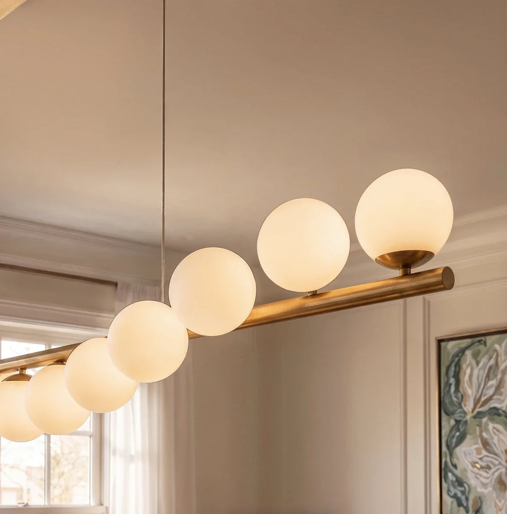 Close view of Clérachic opal white glass globes on a brushed brass bar, each seated on a small brass cup and glowing softly.