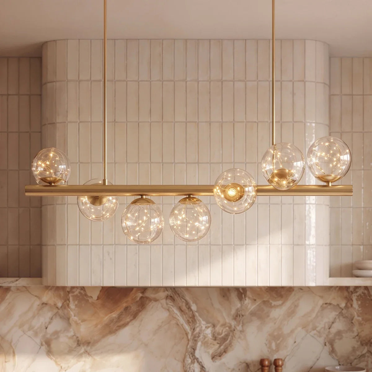 Close view of Clérachic clear glass globes filled with tiny warm lights, mounted on a brass bar with slim brass suspension rods.