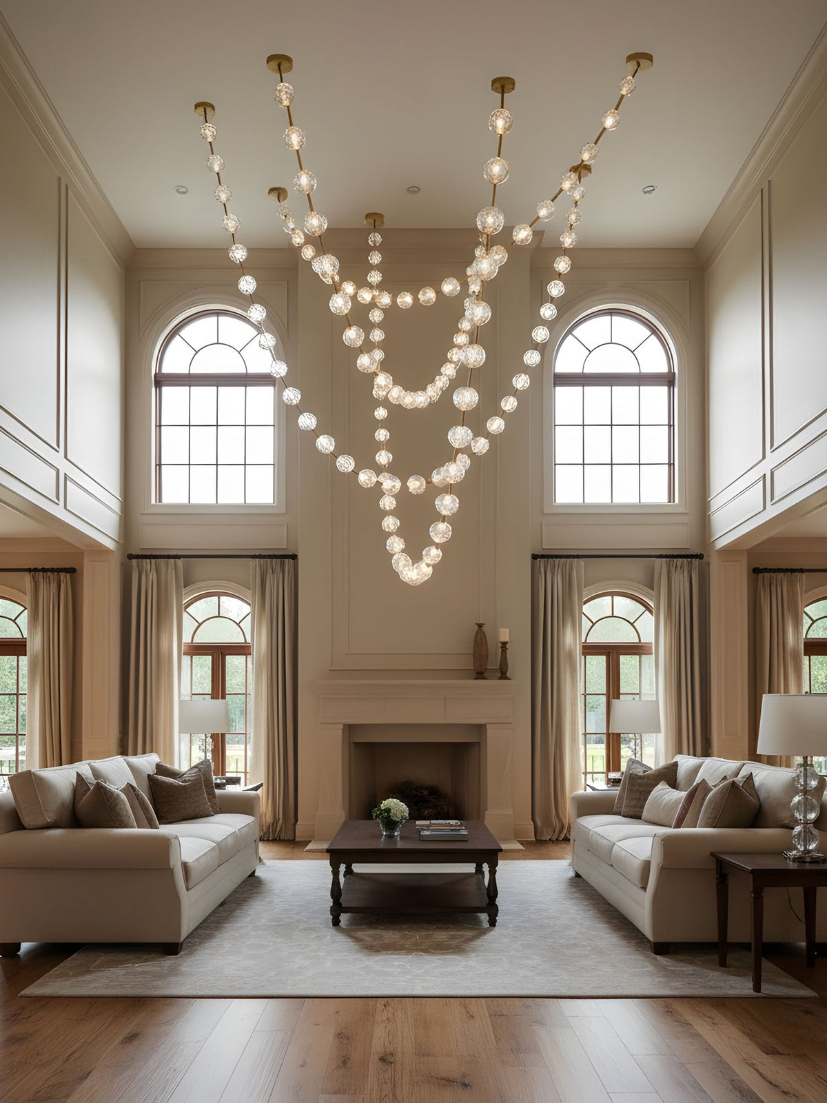 Lit strands of spheres hang below a tall ceiling between arched windows, with two sofas facing a fireplace beneath this Clérachic pendant.