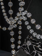Close view of clear patterned spheres and gold connectors on crossing strands of this Clérachic pendant, with a dark reflective sculpture below.