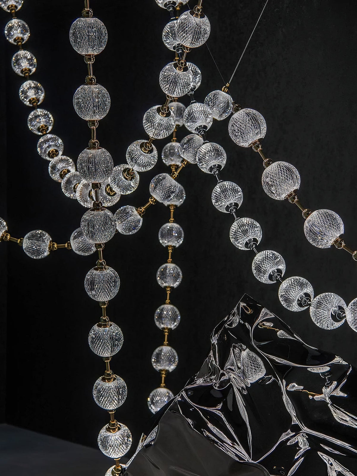 Close view of clear patterned spheres and gold connectors on crossing strands of this Clérachic pendant, with a dark reflective sculpture below.