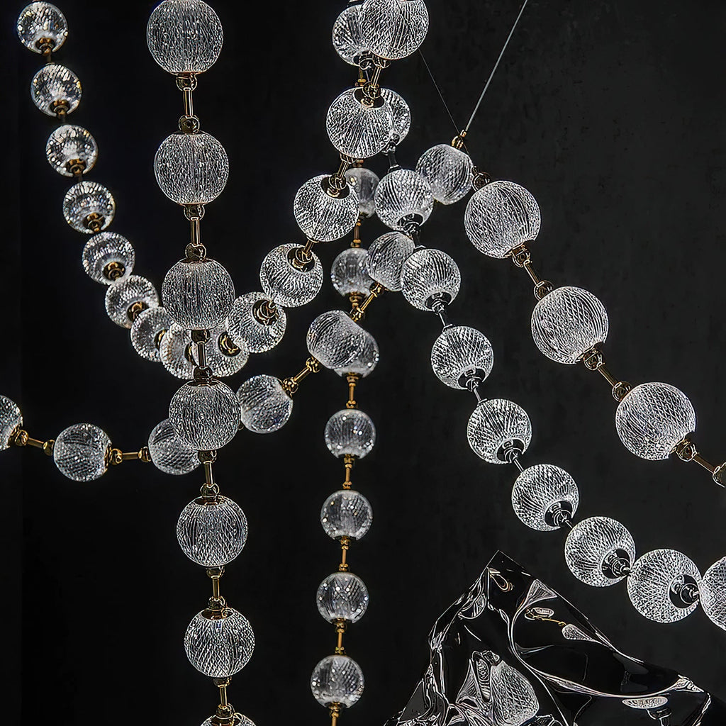 Close view of the cut-pattern glass spheres and slim brass rods where several strands of this Clérachic pendant cross against a black wall.