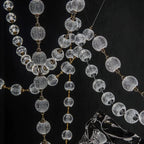 Close view of the cut-pattern glass spheres and slim brass rods where several strands of this Clérachic pendant cross against a black wall.