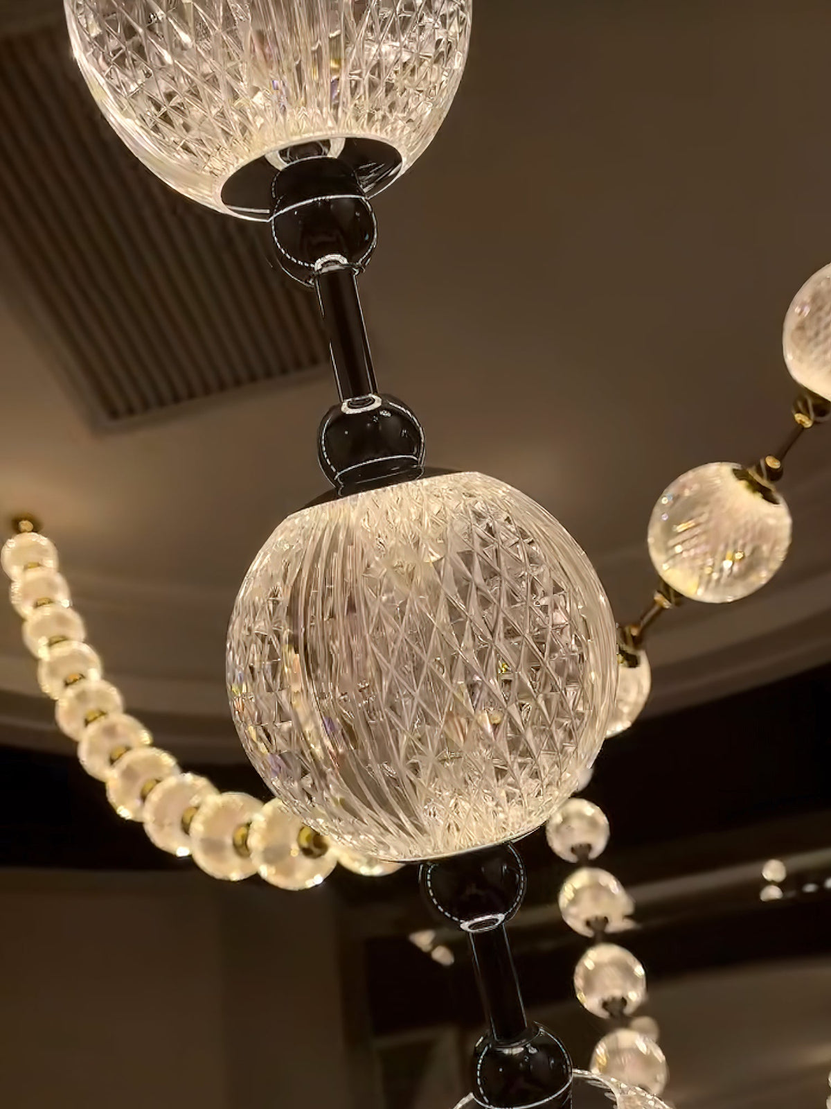 Close-up of one large cut-glass sphere with a dark metal rod between smaller warm-lit spheres on this Clérachic pendant.