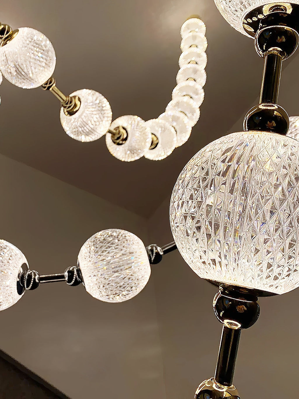 Detail of a large faceted glass sphere beside a string of smaller frosted beads, with dark metal connectors, on this Clérachic pendant.
