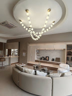 This Clérachic pendant hangs from a round recessed ceiling above a curved cream sofa in an open-plan room, its two lit strands meeting in a deep loop.
