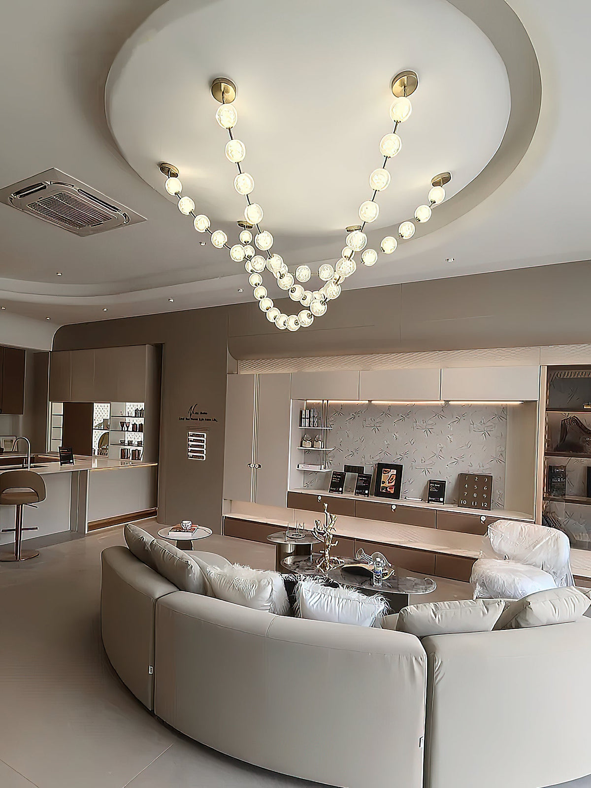 This Clérachic pendant hangs from a round recessed ceiling above a curved cream sofa in an open-plan room, its two lit strands meeting in a deep loop.