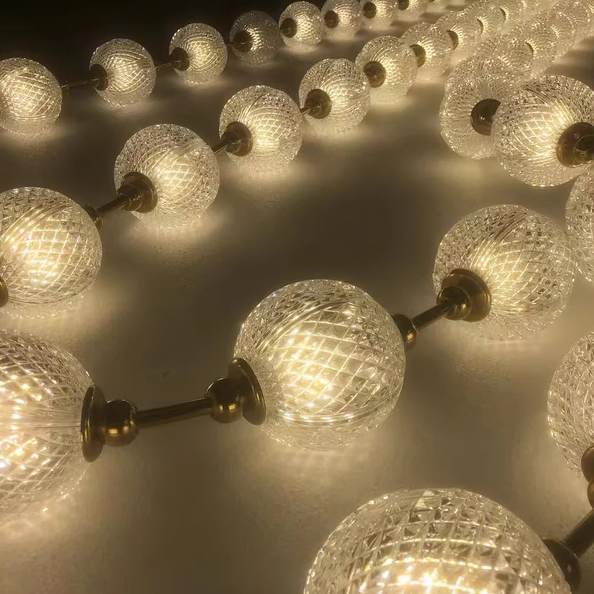 Close view of warm-lit spheres with a diamond lattice pattern, joined by short brass rods, on this Clérachic pendant.