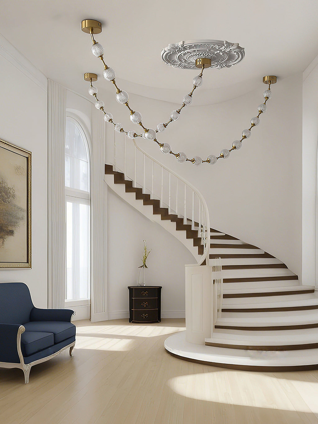 Gold-linked spheres on this Clérachic pendant swoop below an ornate ceiling rose beside a spiral staircase with dark treads and a navy armchair.