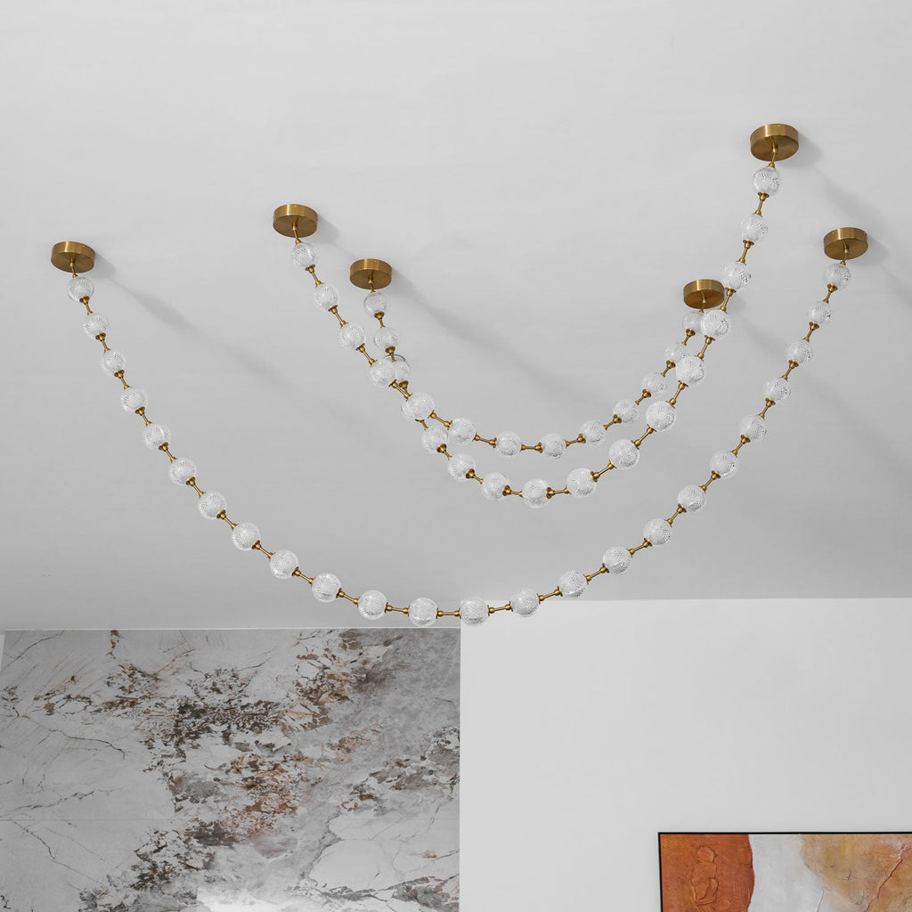 Looking up at unlit frosted spheres on gold links, with this Clérachic pendant's round brass ceiling plates fixed to a white ceiling.