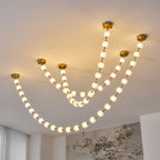 Lit warm white, this Clérachic pendant shows six strands of different lengths from separate brass plates, with a marble wall behind.
