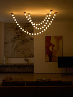 At dusk the glowing strands of this Clérachic pendant hang above a low marble ledge, a framed abstract painting and a dark sofa.