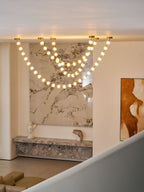 Warm-lit spheres on this Clérachic pendant loop down from the ceiling edge of a mezzanine, above a stone shelf, a small bust and a red-toned painting.