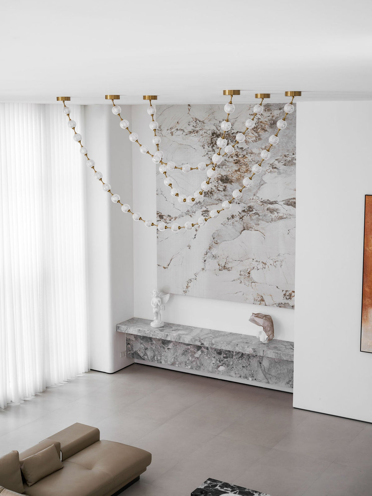 A wide room view shows the unlit strands of this Clérachic pendant against a marble wall, above a stone ledge and a low taupe sofa.