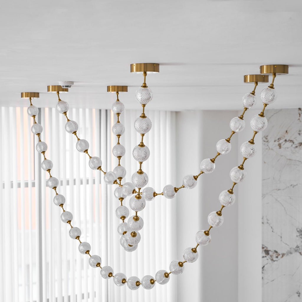 Looking up, frosted and cut-pattern spheres on gold links drape in several loops across sheer white curtains on this Clérachic pendant.