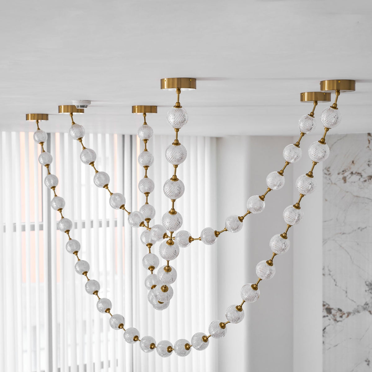 Looking up, frosted and cut-pattern spheres on gold links drape in several loops across sheer white curtains on this Clérachic pendant.