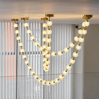 Glowing warm-white spheres in several overlapping loops hang in front of vertical blinds, a strong light from this Clérachic pendant.