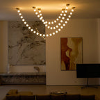 Lit strands of spheres hang in dusk light over a marble wall and a red-and-ochre painting, with a black TV stand at right, from this Clérachic pendant.