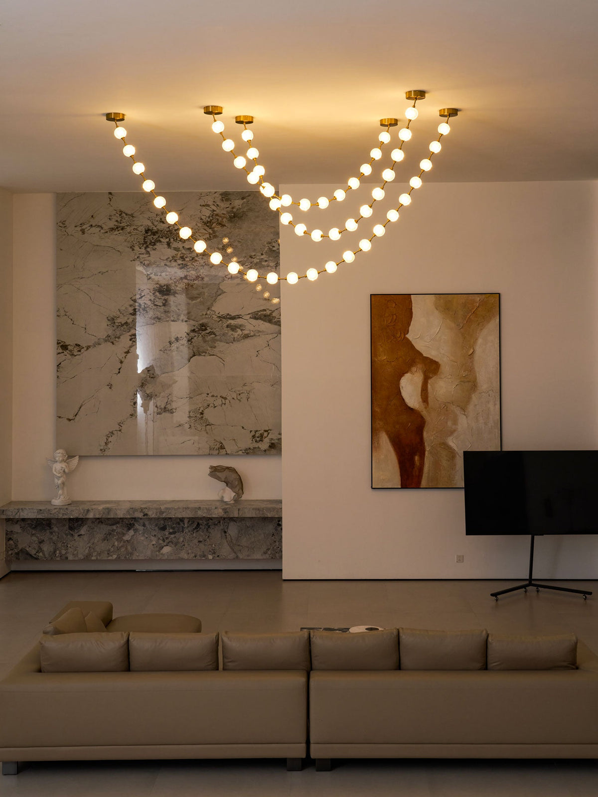 A wider view of this Clérachic pendant lit at dusk above a marble wall, a low ledge, a flat-screen TV and a taupe sofa.