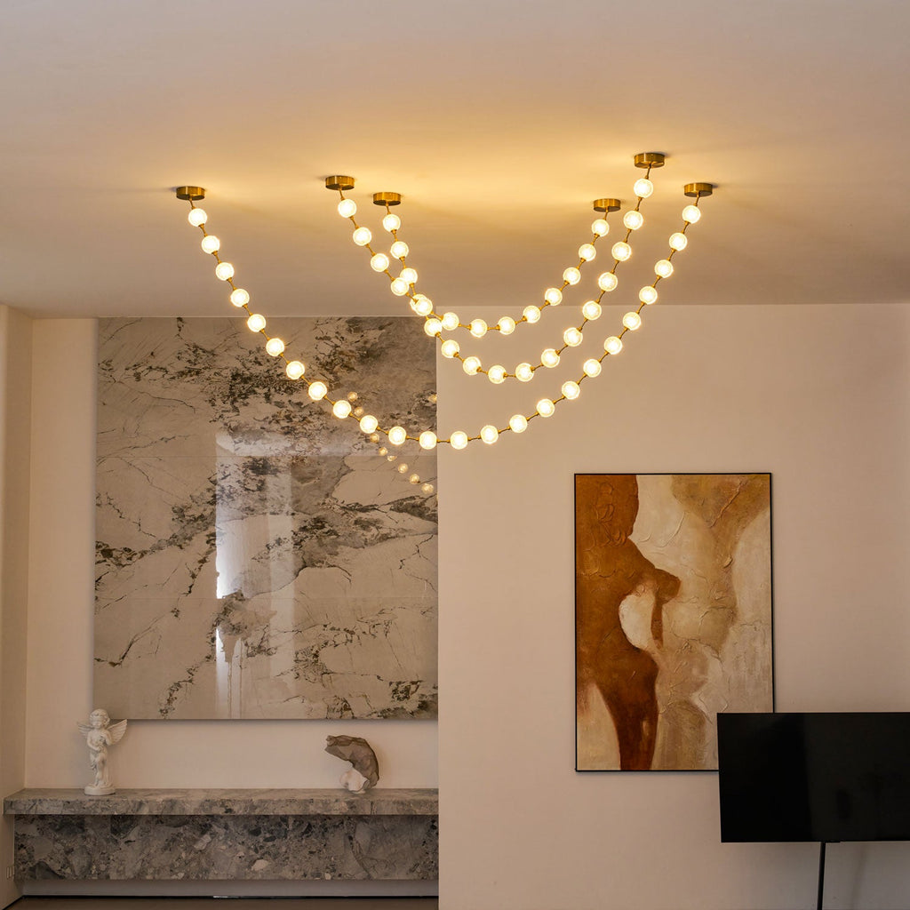 Three glowing swags from this Clérachic pendant hang beside a marble wall and a painting in rust and cream, with a black TV stand to the right.