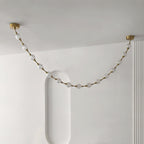 Looking up, a single swag of frosted spheres on gold rods spans a white ceiling between two brass plates, from this Clérachic pendant.