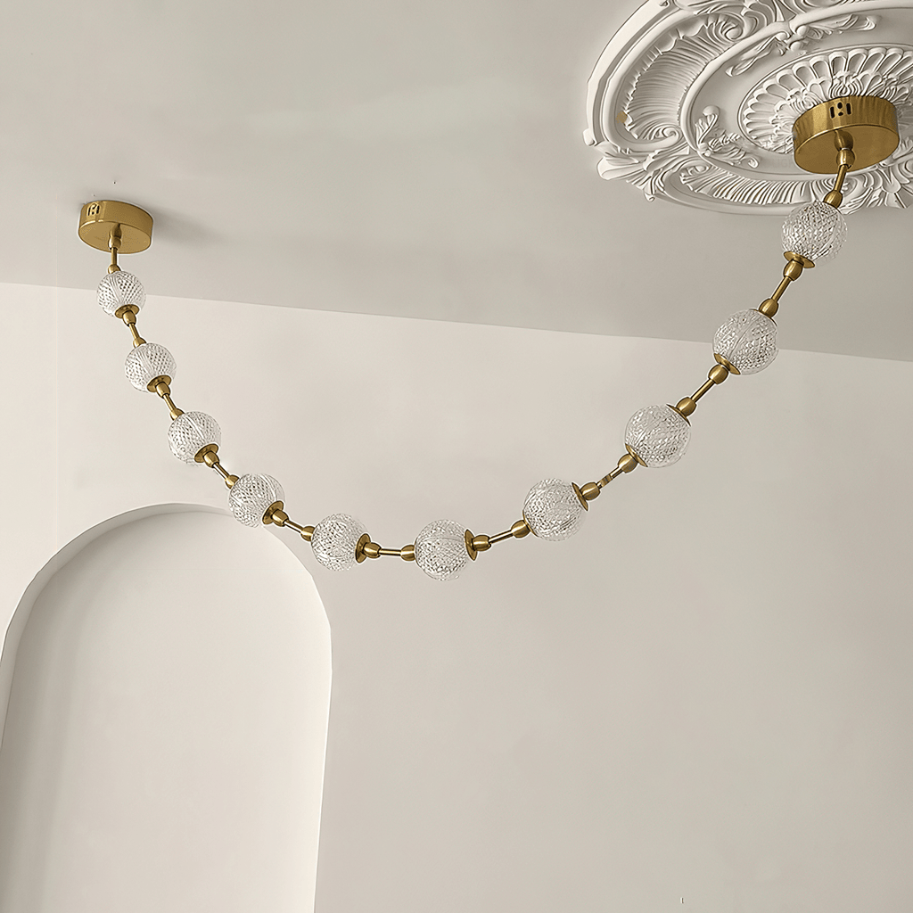 Close view of a swag of cut-pattern spheres hanging from a brass plate beside an ornate plaster ceiling rose, on this Clérachic pendant.