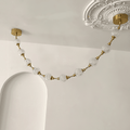 Close view of a swag of cut-pattern spheres hanging from a brass plate beside an ornate plaster ceiling rose, on this Clérachic pendant.
