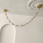 Close view of a swag of cut-pattern spheres hanging from a brass plate beside an ornate plaster ceiling rose, on this Clérachic pendant.