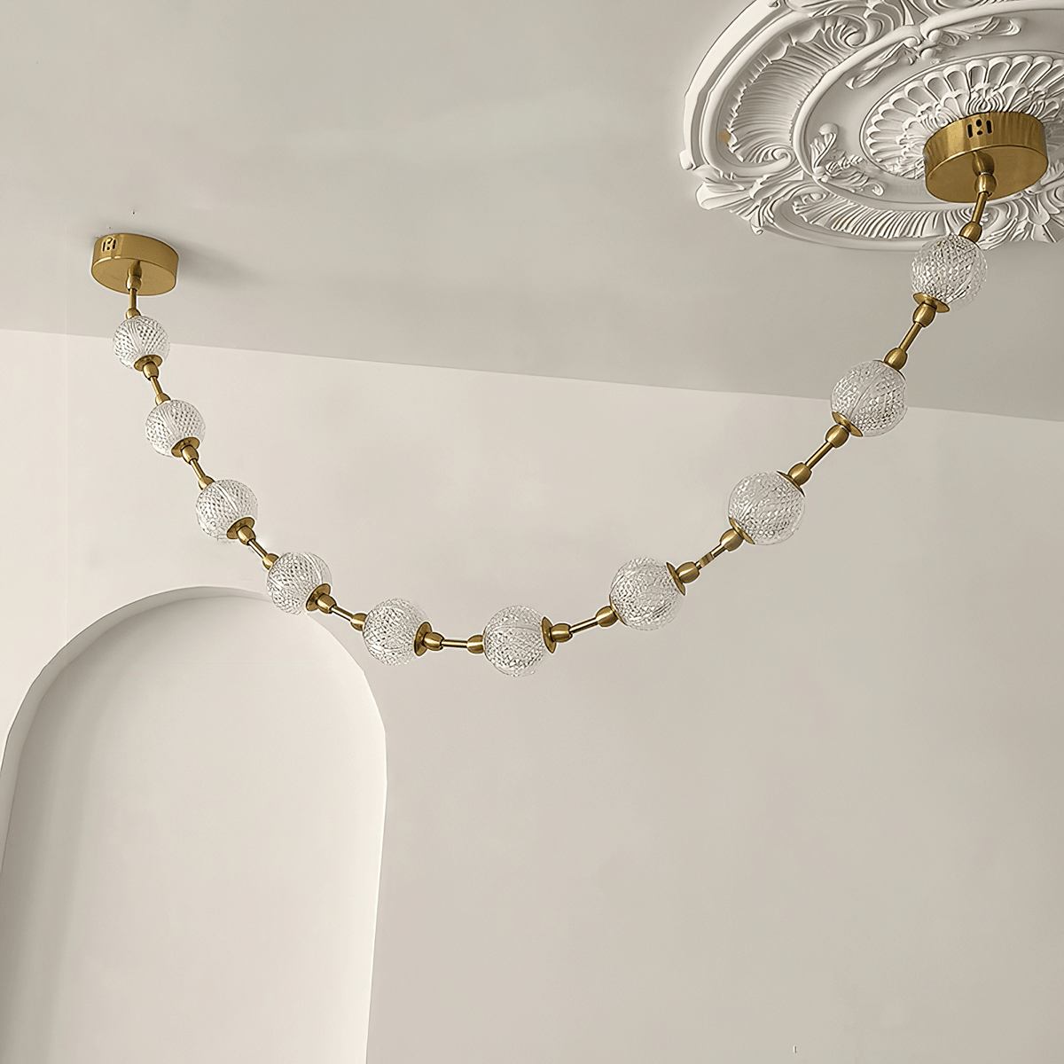 Close view of a swag of cut-pattern spheres hanging from a brass plate beside an ornate plaster ceiling rose, on this Clérachic pendant.