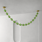 Green spheres on gold rods make one swag across a pale grey ceiling beside a rounded niche, in the Gold & Green version of this Clérachic pendant.