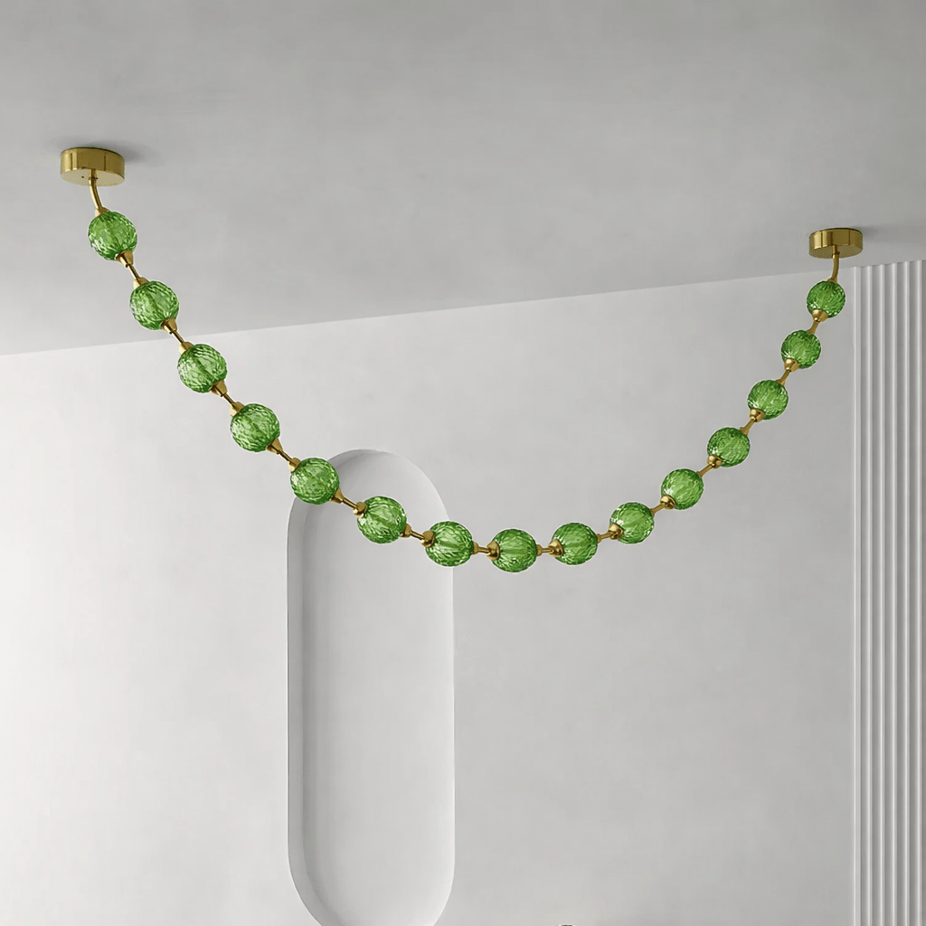 Green spheres on gold rods make one swag across a pale grey ceiling beside a rounded niche, in the Gold & Green version of this Clérachic pendant.