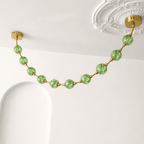 Close view of green crackle-glass spheres on gold rods beside an ornate ceiling rose, on this Clérachic pendant in green.