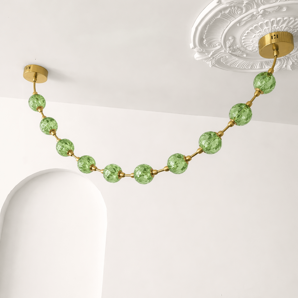 Close view of green crackle-glass spheres on gold rods beside an ornate ceiling rose, on this Clérachic pendant in green.