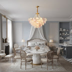 A Clérachic tiered glass-disc pendant lights a pale blue dining room with a marble table, cane-back chairs and a draped bed beyond.