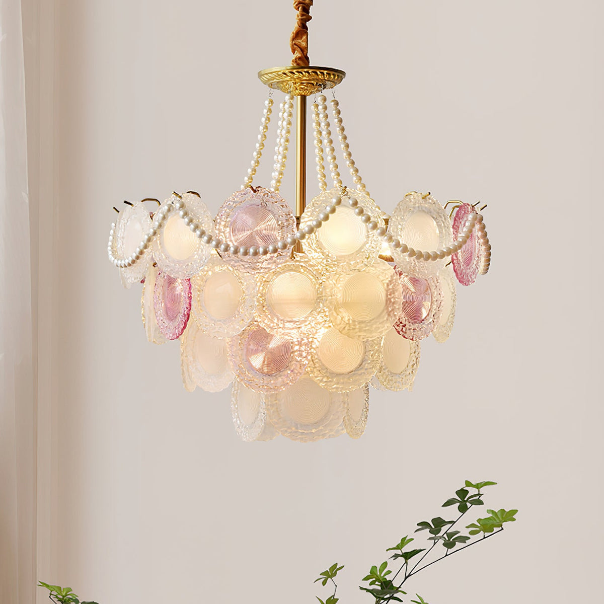 This Clérachic pendant glows warm on a pale wall, its pearl swags looping over rows of rose-tinted and frosted glass discs.