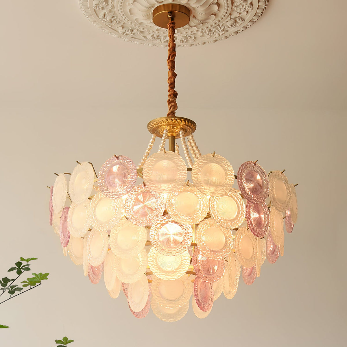 Close upward view of a lit Clérachic pendant under a ceiling rose, showing the textured glass discs and the gold canopy.