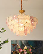 A lit Clérachic pendant with layered pink and white discs, a pearl swag and a gold canopy, with a painting of roses below.