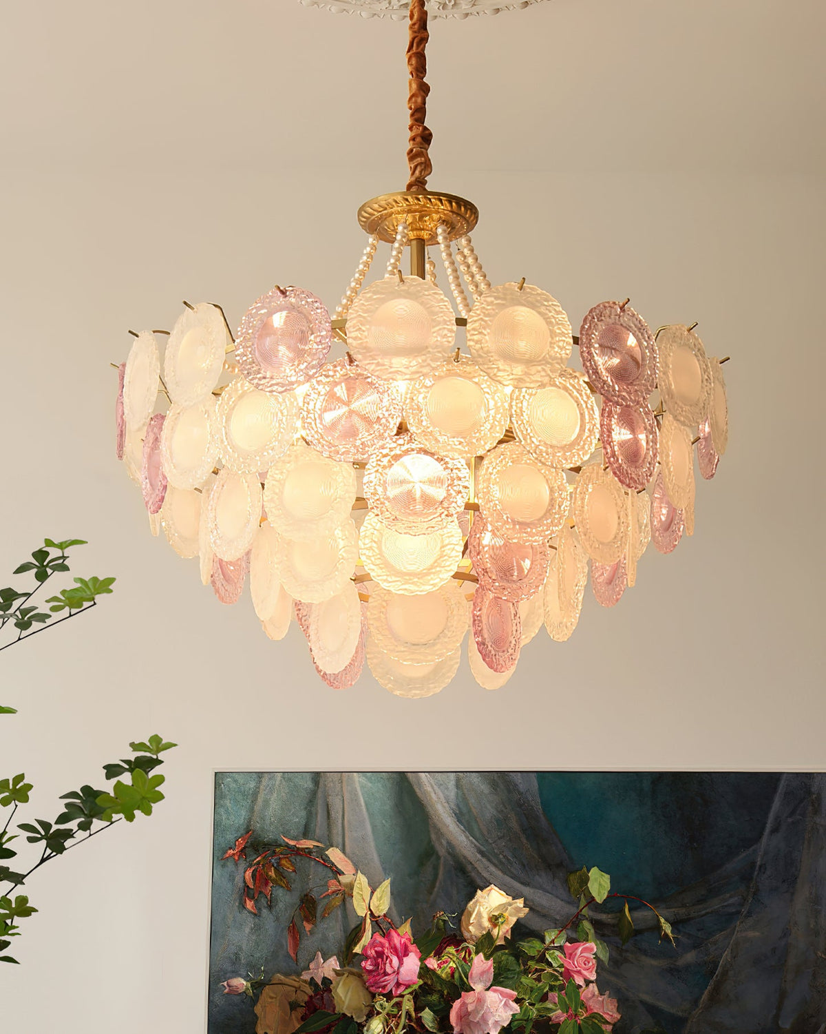 A lit Clérachic pendant with layered pink and white discs, a pearl swag and a gold canopy, with a painting of roses below.