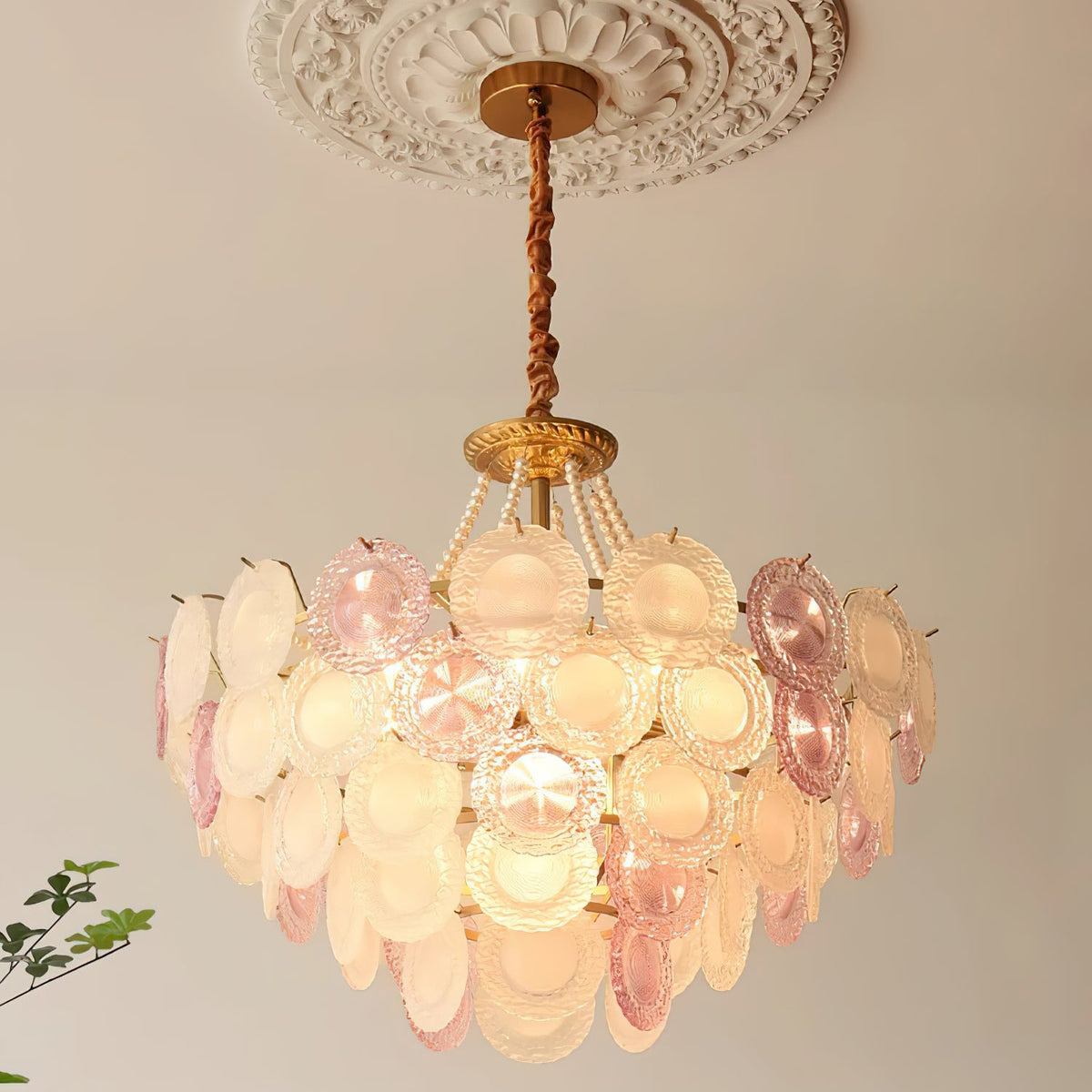 This Clérachic pendant lit under a ceiling rose, with warm light behind the pink and frosted discs and the pearls above them.