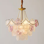 A Clérachic pendant with a narrower profile, lit, showing pearl swags, a gold canopy and pink-and-white glass discs.