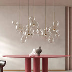 A cluster of Clérachic clear glass sphere pendants with gold stems, hung over a dusty-red round dining table.