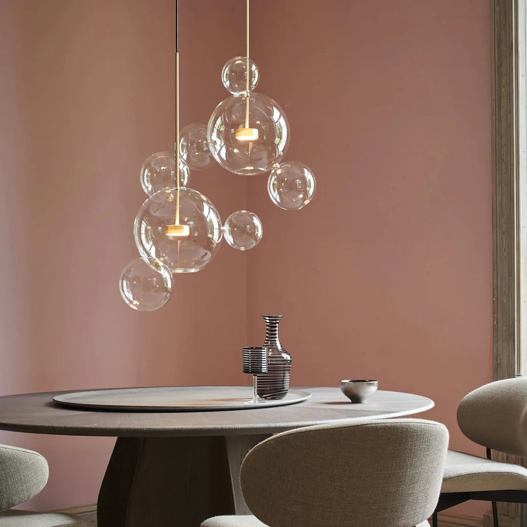 Clérachic glass sphere pendant with small spheres at different heights, against a dusty-pink wall above a round table.