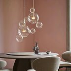 Clérachic glass sphere pendant with small spheres at different heights, against a dusty-pink wall above a round table.