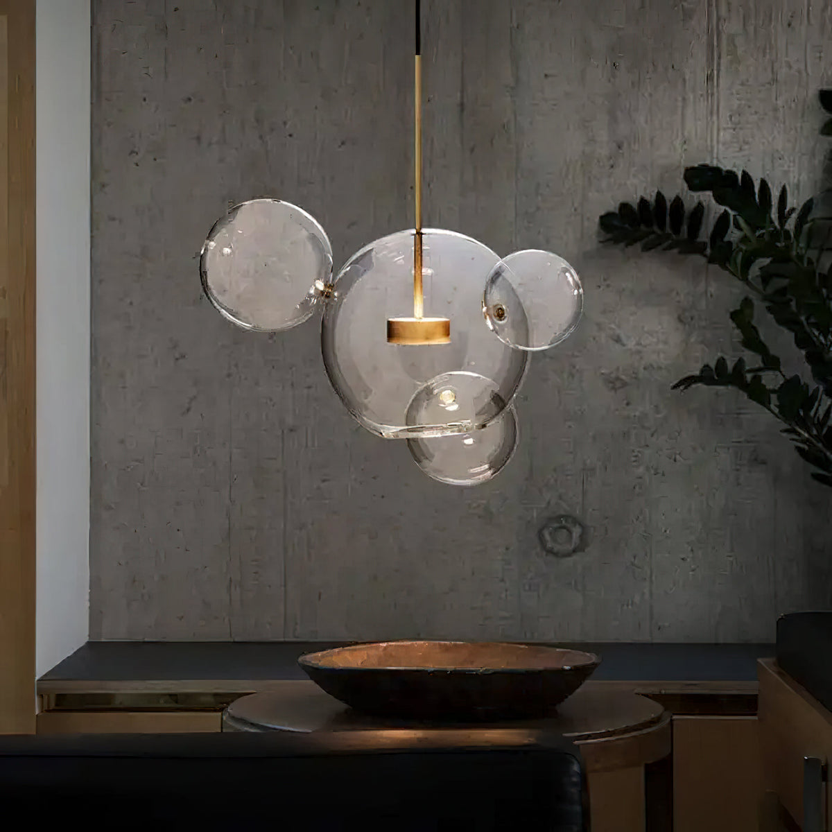 Single Clérachic glass sphere pendant with clear satellite spheres, against a rough concrete wall beside a large plant.