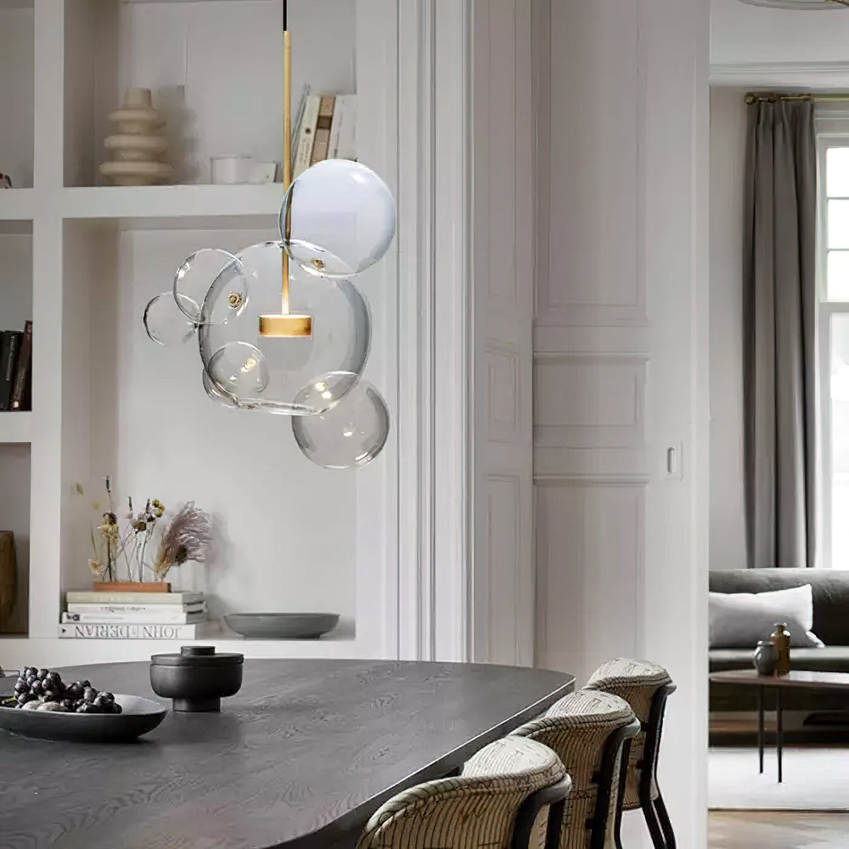 Lit Clérachic clear glass sphere pendant in a white room with built-in shelves, above a dark wooden dining table.