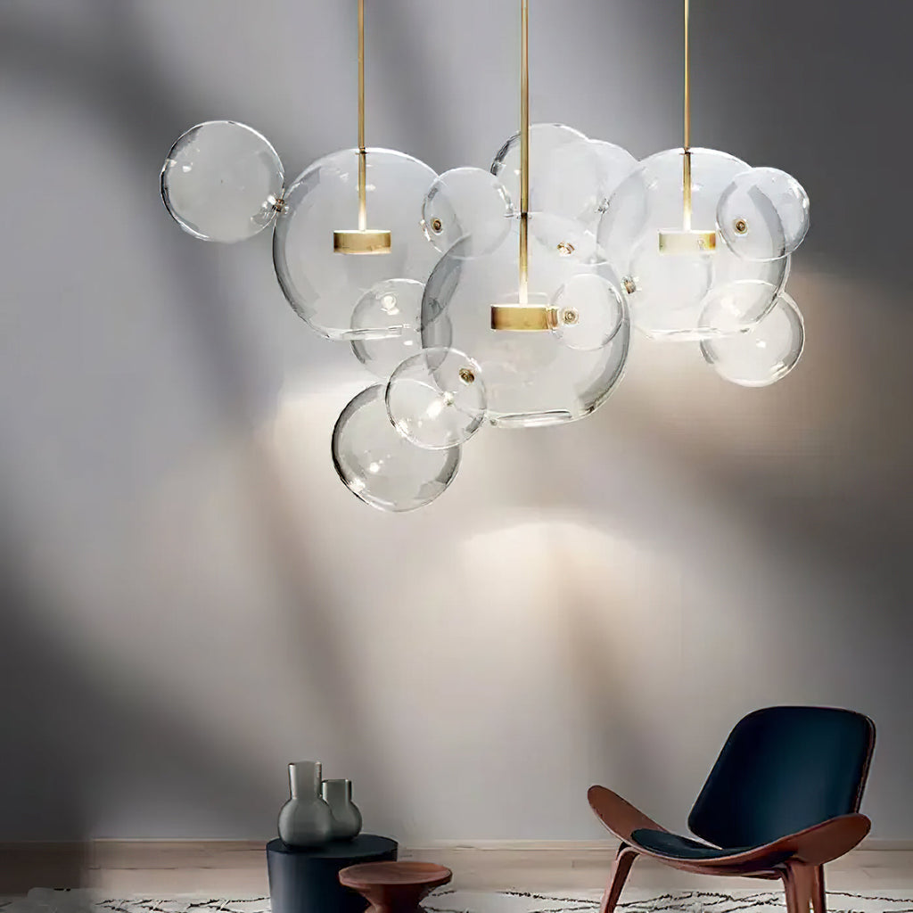 Clérachic clear glass sphere pendants casting soft patterns on a grey wall above a wooden lounge chair.